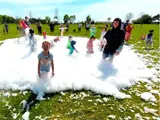 Kids are playing in a large pile of foam on a park lawn.