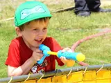 A young boy holds a water gun, and is spraying water over a short barrier