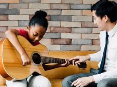 an adult teaching a child to play guitar